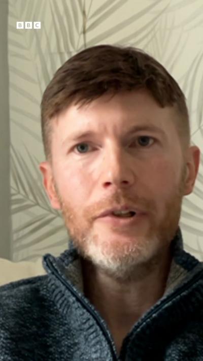 A man with brown hair and beard wearing a blue jumper