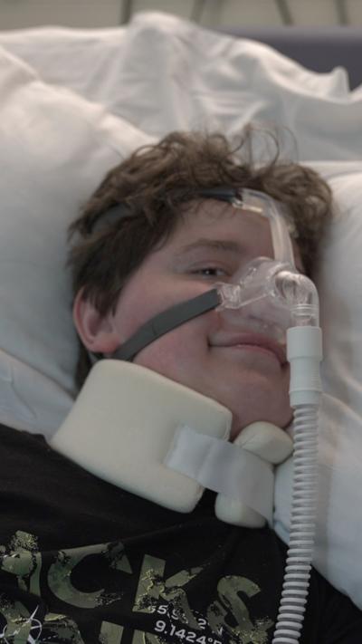 Kyle in his hospital bed. He has a neck brace on and a tube in his nose.