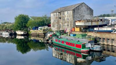 Boats on a canal with buildings behind and the blue sky above reflected in the water