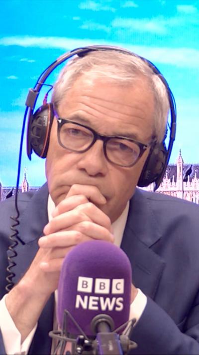 Nigel Farage wears headphones and sits in front of a microphone in a radio studio.