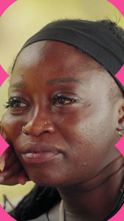 A woman looks reflective while resting her head on her right hand. She wears a black headband 