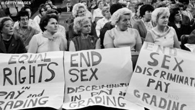 A group of women hold signs calling for equal rights and an end to sex discrimination in pay grading