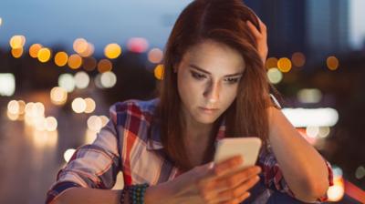 Young woman looks at her mobile phone with city lights in the background