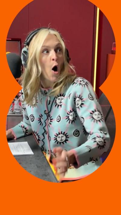 Fearne Cotton has a long blonde hair. She has her mouth open in surprise. She is a wearing a blue patterned cardigan and is seated at a radio desk.
