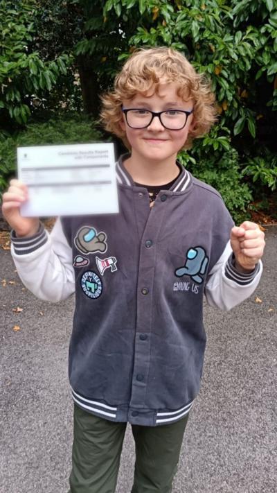 Harry, who is wearing glasses,  holds up his results 