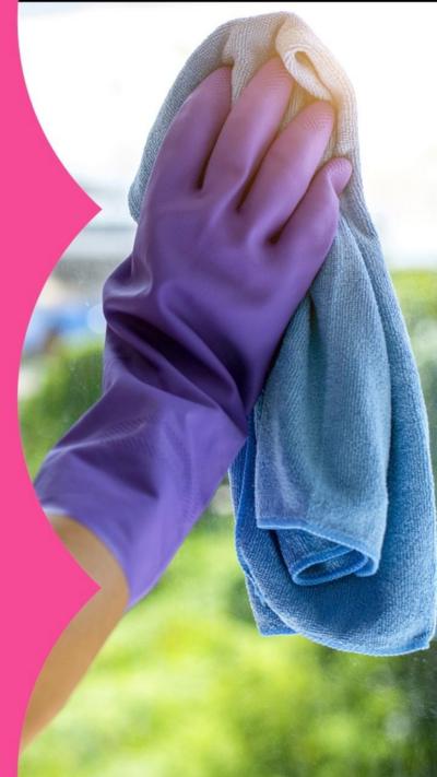 Close-up of a person's arm cleaning a window. Their hand is in a purple glove and they hold a blue cloth.