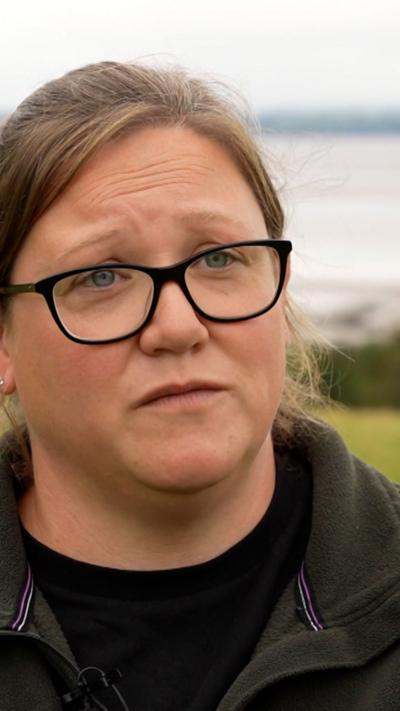 A woman with black rimmed glasses and a brown fleece standing in a field