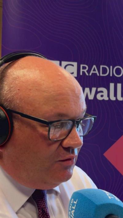 Mark Hopwood sat in from of a BBC Radio Cornwall sign. 