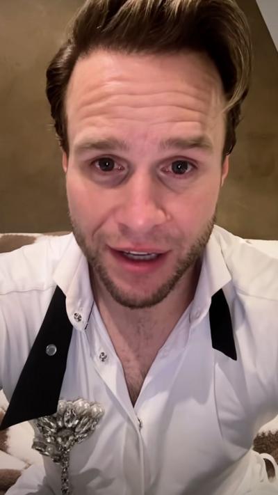 Olly Murs looks directly at the camera, he is wearing a white shirt and black tie