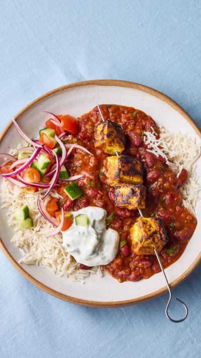 Top-down view of a plate with a tofu skewer sitting a bed of curry and rice