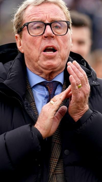 Harry Redknapp wearing his lucky tie. His hands are mid clap and he's shouting looking past the camera and wearing dark rimmed glasses.