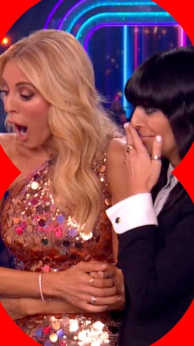 Presenter Tess Daly wearing gold rose dress with sequins standing next to presenter Claudia Winkleman holding hand to her face
