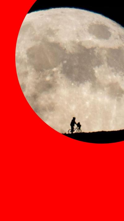 A silhouette of a man pushing a bike in front of a large moon