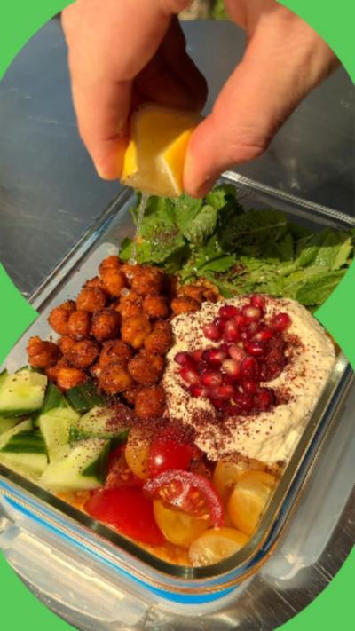 Harissa couscous with crispy chickpeas in a food storage container with a lemon being squeezed on top of it