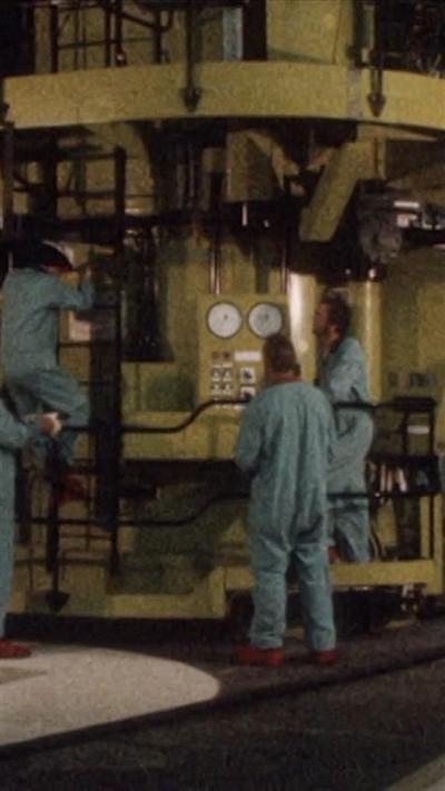 Three men in pale blue boiler suits standing in front of a piece of machinery at Hinkley Point B