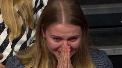 Woman with blond hair crying as she clasps her hands in front of her face