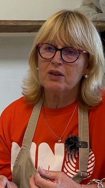 A woman wearing a pottery apron talking to the camera