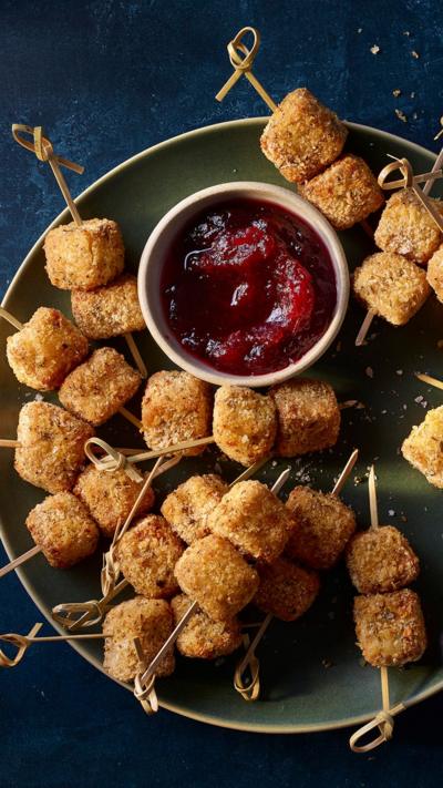 Top down view of tofu bites on wooden skewers next to a small bowl or cranberry dip