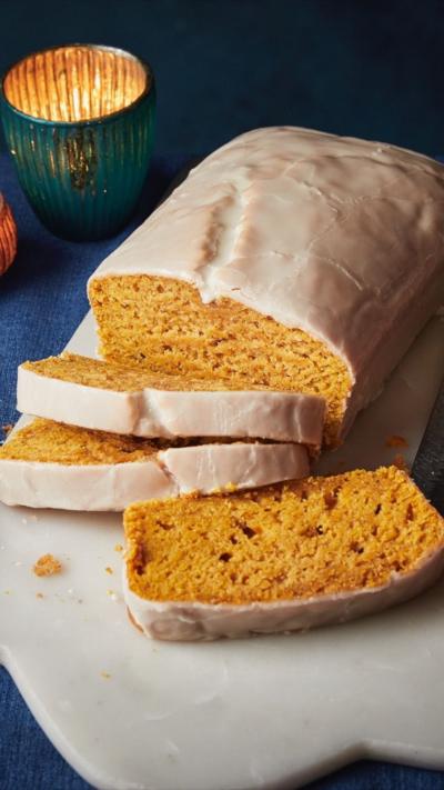 Iced loaf with some slices already cut sitting on a white chopping board