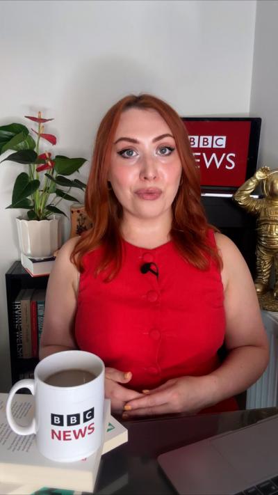 BBC journalist Alice Cruickshank - a young woman with shoulder length red hair, seated and wearing a red top