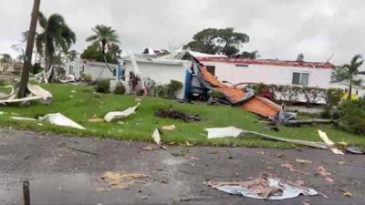 A house's roof has been torn off and debris litters the surrounding area