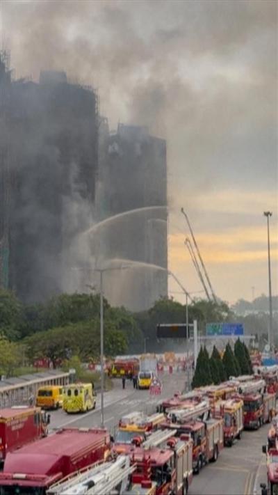 Red fire engines are seen in front of four smoking apartment blocks. 