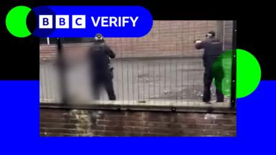 Two police officers are seen pointing their weapons at a man lying on the ground who is blurred