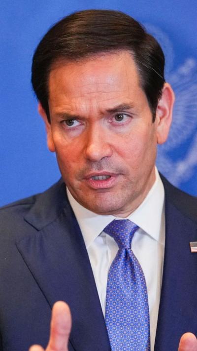 Marco Rubio looking at camera wearing a navy suit and blue tie