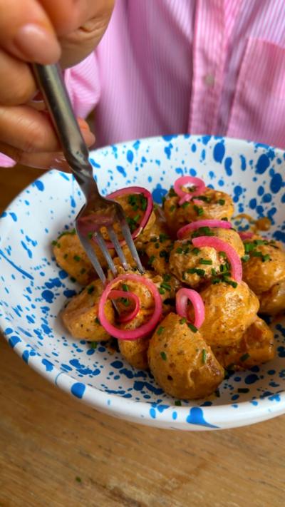 A fork is shown dipping in to a bowl of piri-piri potatoes topped with pink onions.