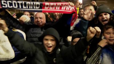 Group of cheering fans with a scarf raised reading "Scotland/Denmark"