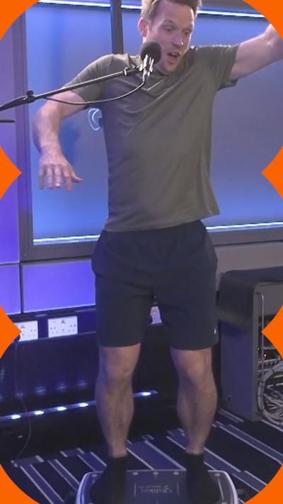 A man in shorts and a t-shirt stands on a vibration plate