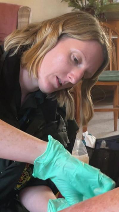 A paramedic wearing a green glove is carefully tending to a patient's arm in a home setting.
