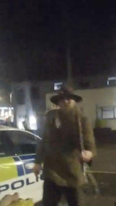 Man standing at the door to a police station, with a weapon in his hands.