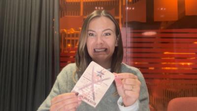 Reporter Tink Llewellyn grimacing while holding a lottery tickets with a big cross through it