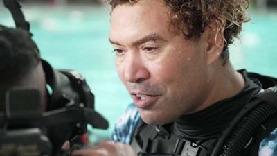 Curly the diving instructor adjusting a mask in a swimming pool as he teaches