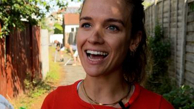 Woman smiles while people clean up alleyway in background