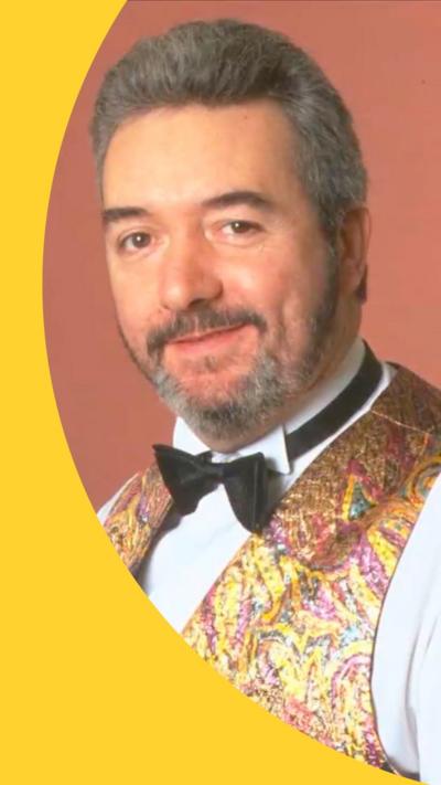 John Virgo, with short grey hair and beard, dressed in a sparkly waistcoat and bow tie