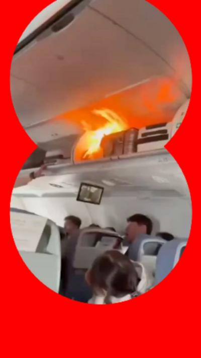 A small fire in an overhead locker inside a plane cabin. People beneath are looking up.