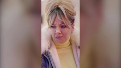 A woman looking disgusted, with blonde hair piled on top of her hair, and a coat with a fluffy collar.