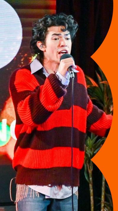 A man, Conan Gray, stands in a red striped top and jeans in the Radio 1 Live Lounge