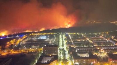Aerial of red flames burning in mountain next to houses