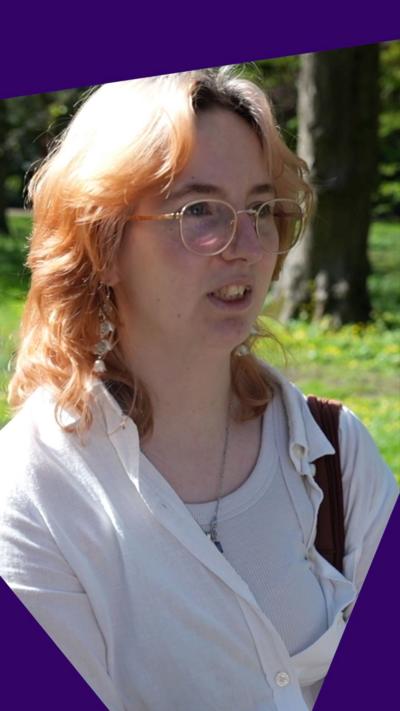 A young woman with blonde hair and glasses looks being interviewed in a park