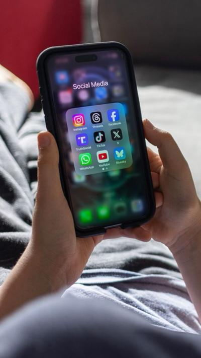 A hand holds up a smartphone with several social media apps on the screen