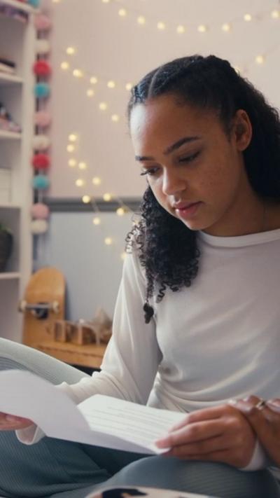 A teenager looks at a sheet of paper in her bedroom.
