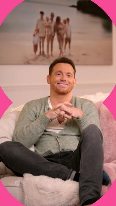 Joe Swash sit son a sofa smiling 