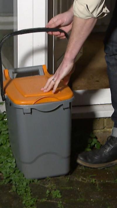 A grey food caddy with an orange lid.