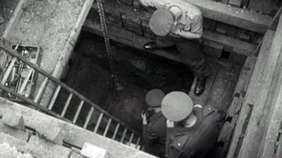 Men look down a tunnel to the unexploded WW2 bomb.