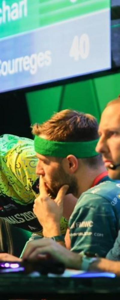 Two men in green T-shirts, one with a headset and another with a green sweatband around his head looking at a spreadsheet