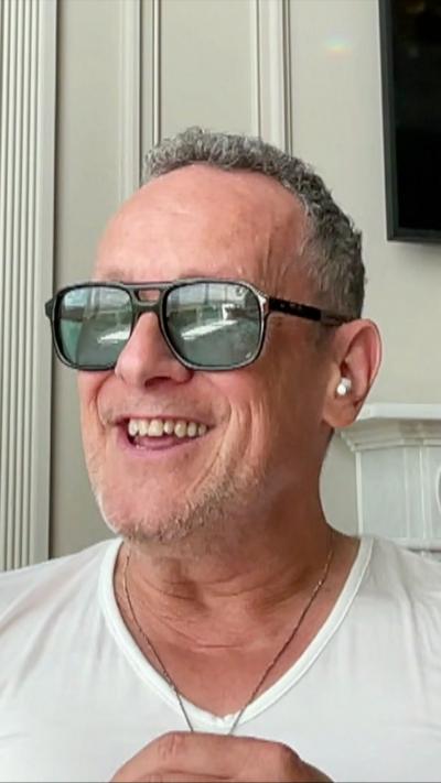 A smiling curly grey haired man with sunglasses on 