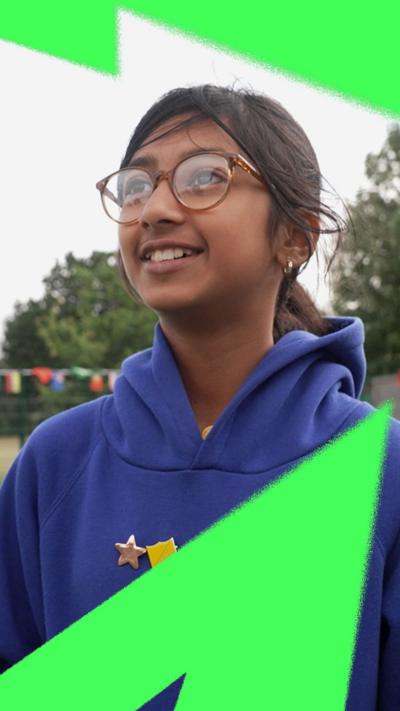 A young girl wearing her blue school uniform with badges on her jumper speaking on a football pitch